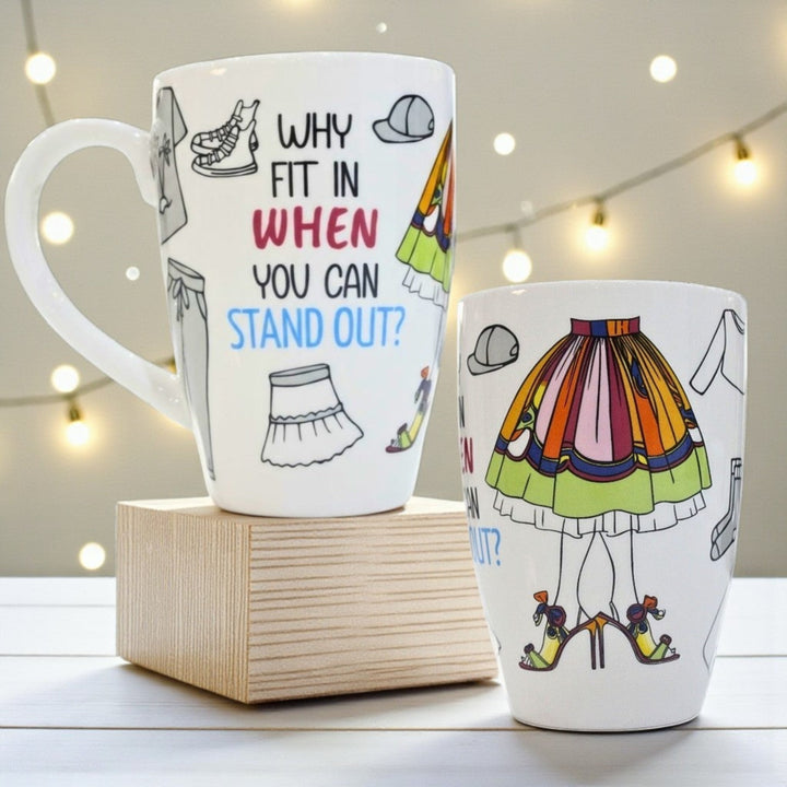 Front and side of a motivational mug with text saying "Why fit In when You can Stand out" and illustrations of black and white as well as colorful clothing.