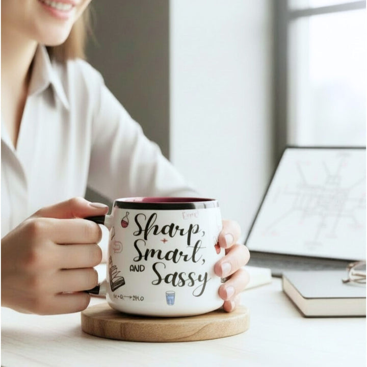 Person holding a mug with 'Sharp, Smart, and Sassy' text in an office setting.